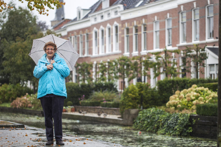 Erfgoedvrijwilliger Alie staat met een paraplu voor een oud gebouw.