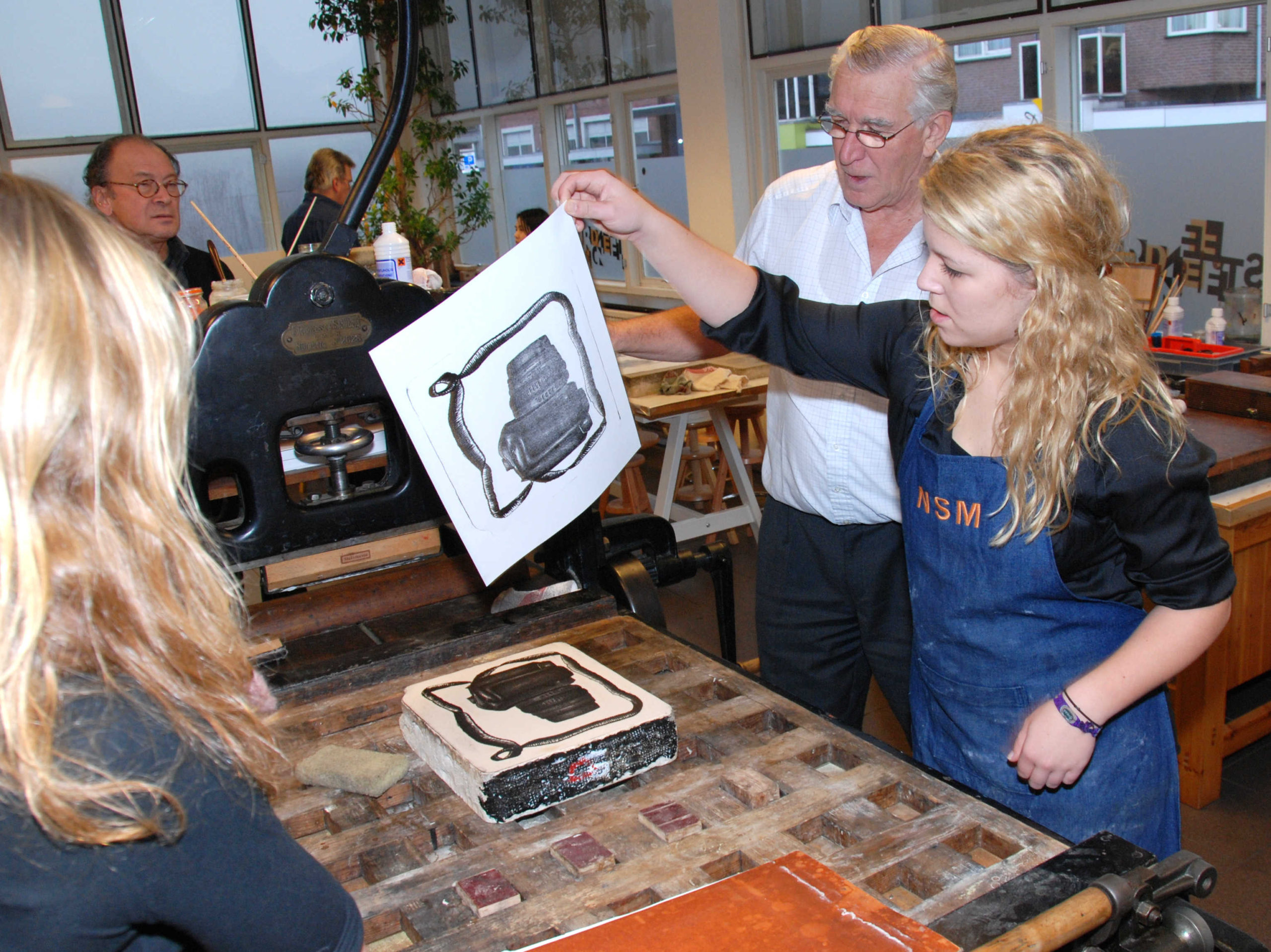 Een workshop in het Nederlands Steendrukmuseum. Eén van de delnemers pakt een stuk papier op, en bekijkt haar drukwerk.
