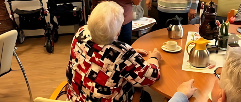 2 mensen opd e rug bekeken, ze zitten aan een tafel met daarop koffie e een ouderwetse kraantjespot